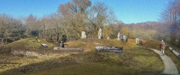 A sunny outdoor scene featuring grassy mounds, trees, and large standing stones. A person sits on a log in the foreground, while another walks along a path to the right. Additional logs are scattered on the ground, and two people are visible near the stones in the distance under a clear blue sky.