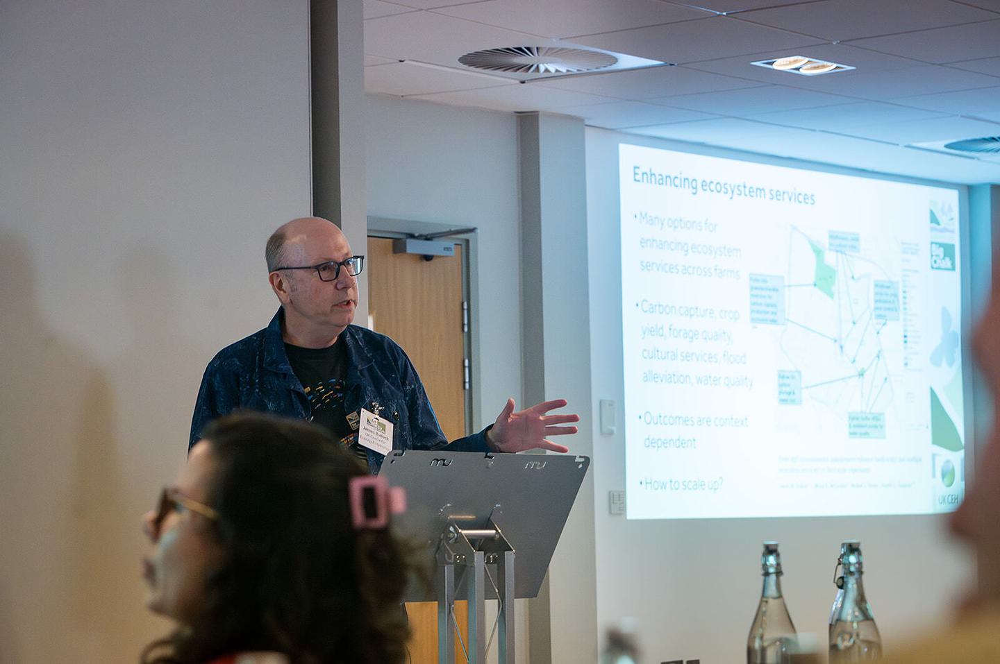 Professor James Bullock speaks at the Big Chalk Conference, highlighting the importance of chalk landscapes and the need for collaboration in their preservation. Attendees listen attentively to his expert insights.