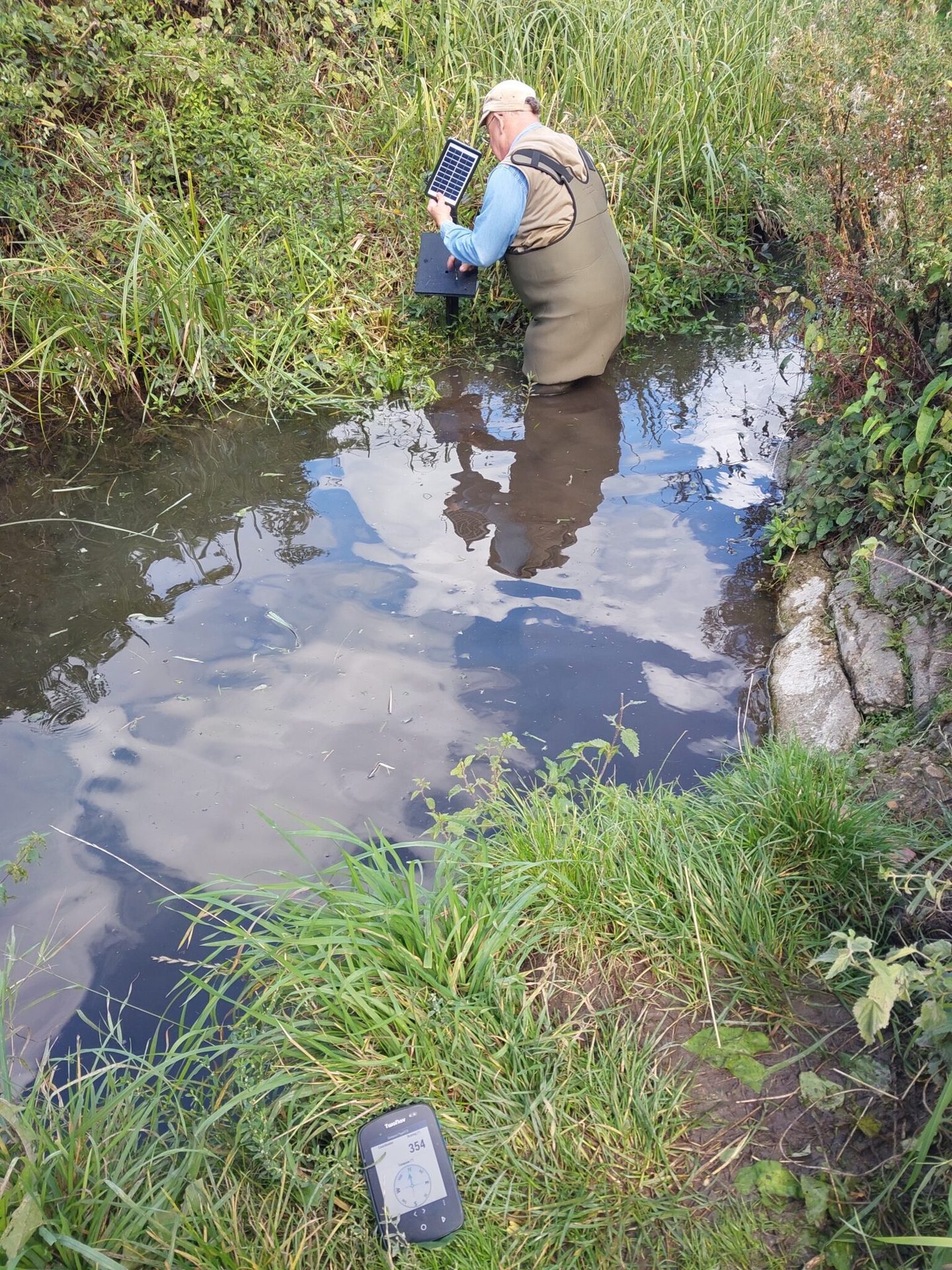 Fieldwork at Cherry Hinton Brook outfall showing deployment of water quality data loggers in a shallow stream. Image highlights environmental monitoring techniques for assessing chalk stream health.