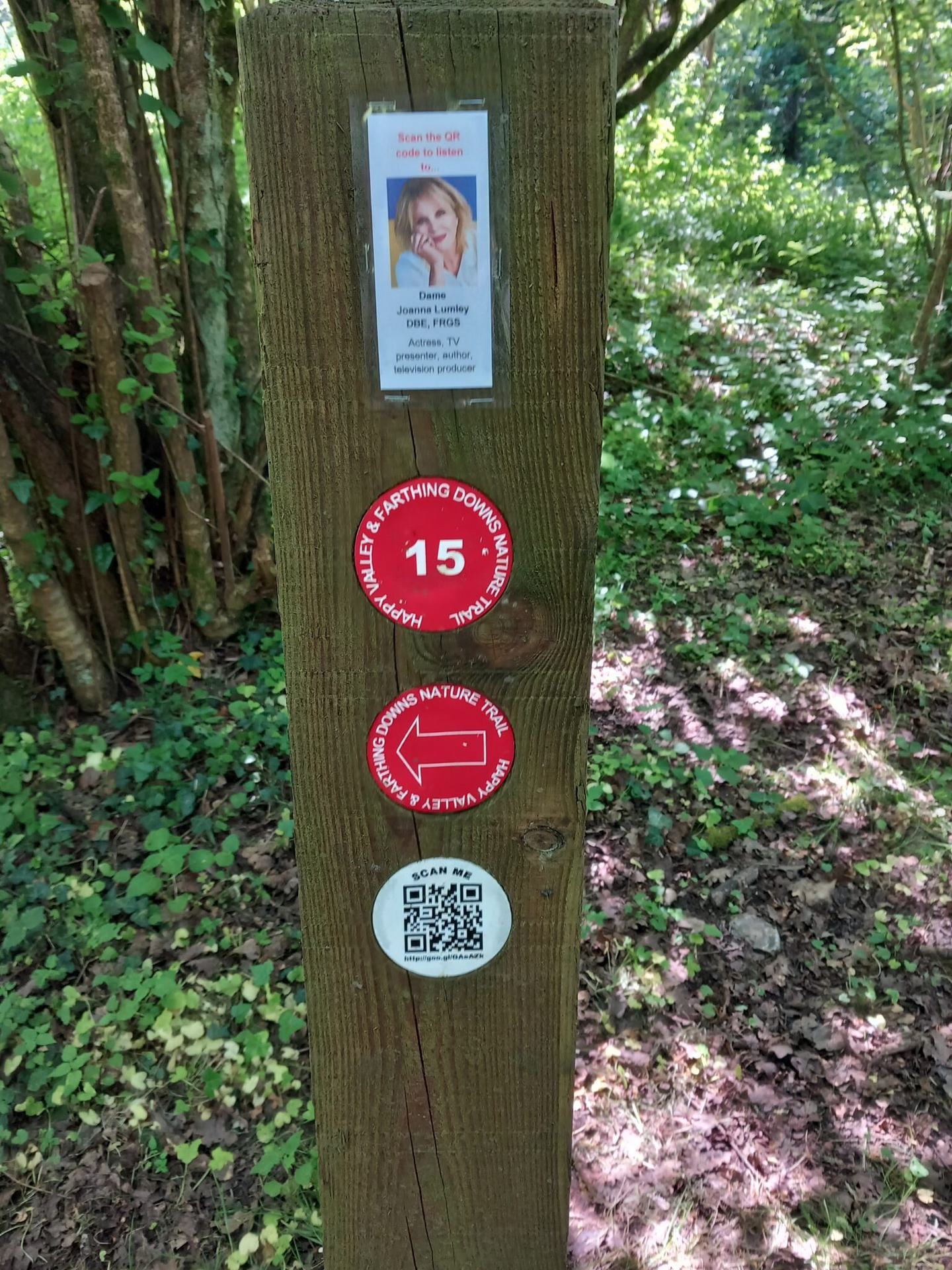 A wooden post with trail wayfinding markers and a QR code to scan, promoting the nature trail podcast voiced by Joanna Lumley.