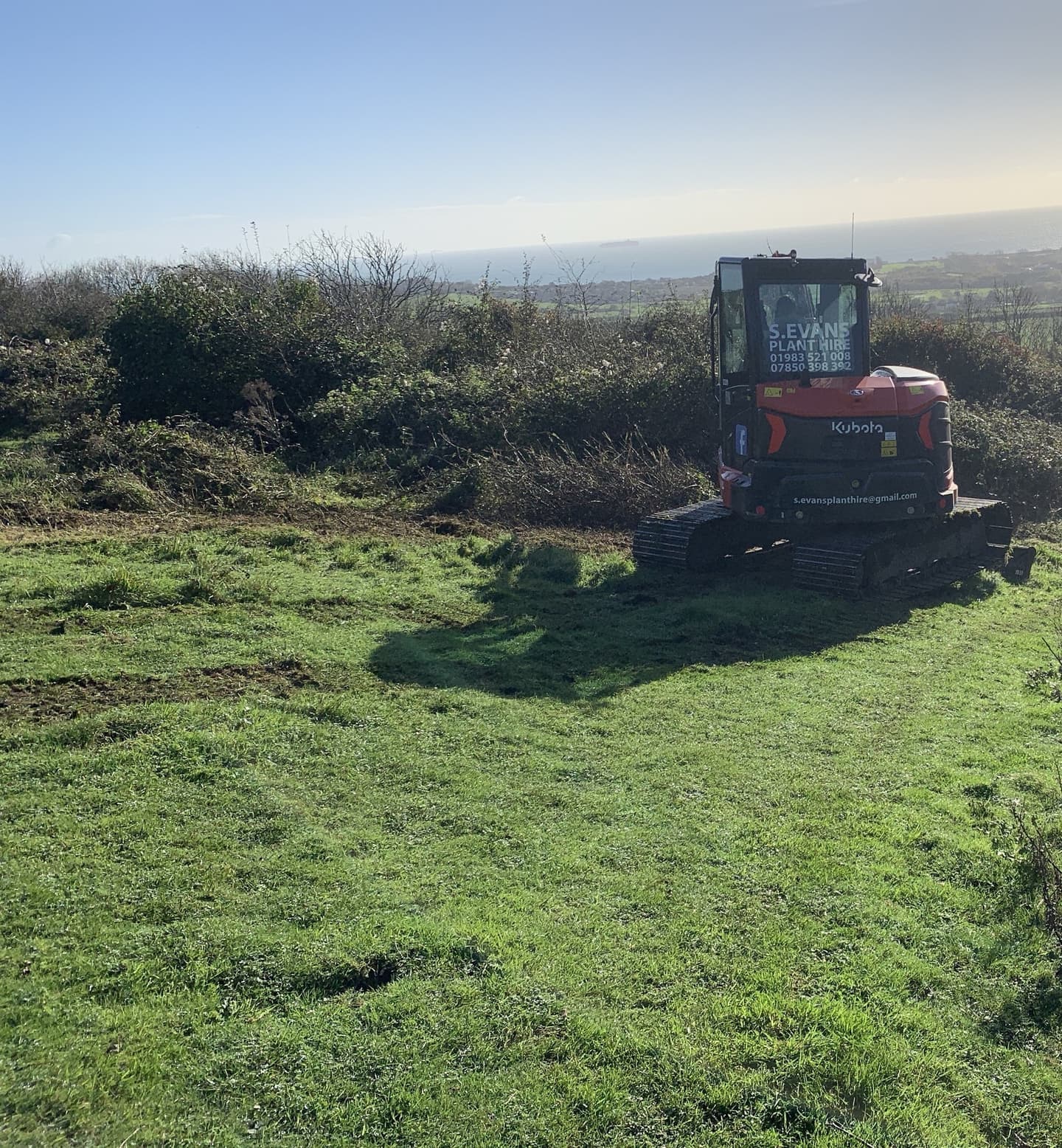 A tractor clearing scrubland at Brading Down, with a backdrop of open countryside and scattered vegetation being removed to restore the landscape.
